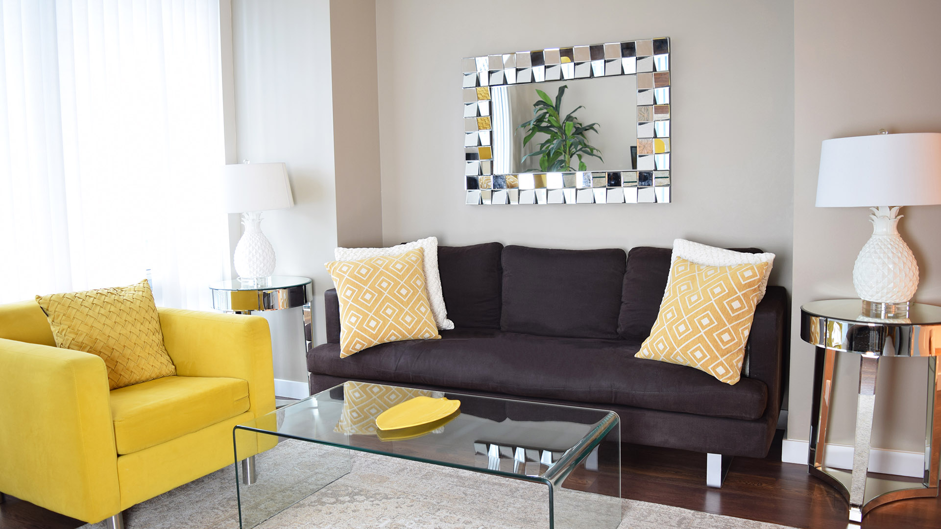 Brown sofa, yellow accent chair, and a wall mirror in the living room of apartment 1003-1288 West Georgia, at the Residences on Georgia.
